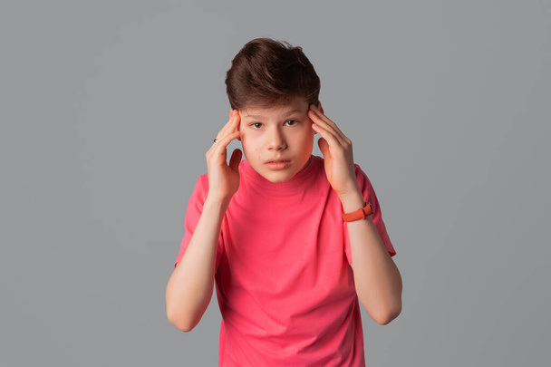 adolescent déçu garçon en t-shirt rose décontracté, regard confus, debout sur fond gris - Photo, image