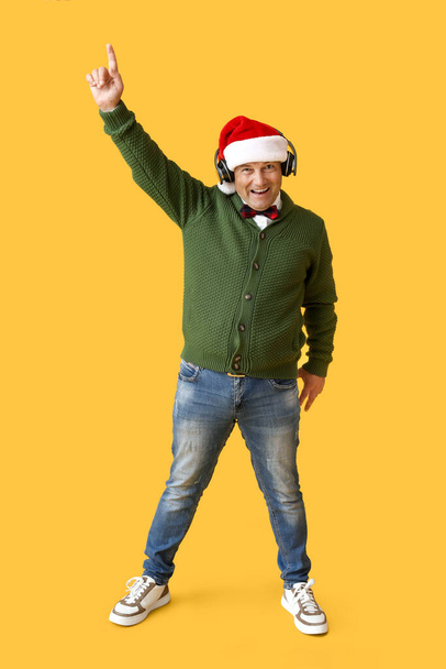 volwassen man luisteren naar kerstmuziek op kleur achtergrond - Foto, afbeelding