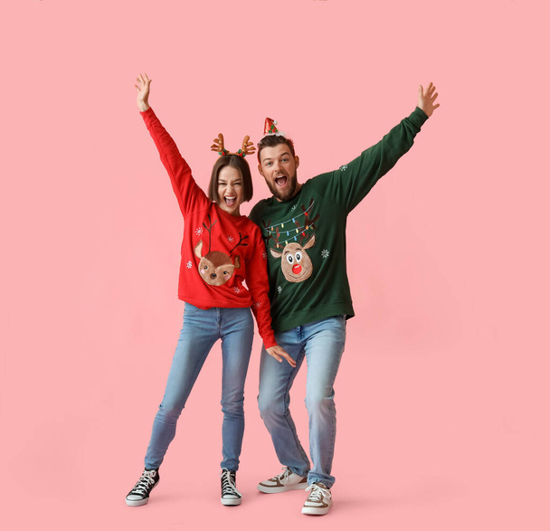 Glückliches junges Paar in stilvoller Weihnachtskleidung auf farbigem Hintergrund - Foto, Bild
