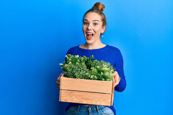 Young blonde woman holding wooden plant pot celebrating crazy and amazed for success with open eyes screaming excited.  - Foto, Bild