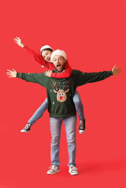 Happy young couple in stylish Christmas clothes on color background - Foto, Imagem