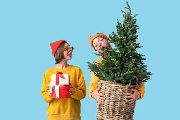 Young couple in stylish winter clothes, with Christmas tree and gifts on color background - Photo, Image