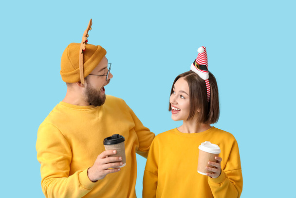 Happy young couple with Christmas decor and cups of coffee on color background - Photo, Image