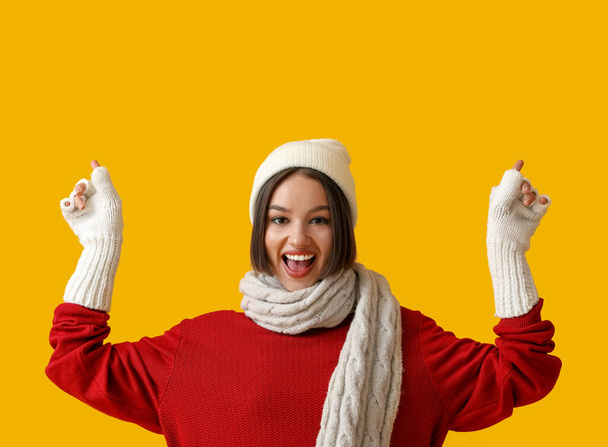 Young woman in stylish winter clothes showing something on color background - Фото, зображення