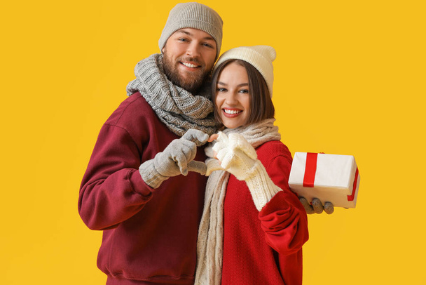 Glückliches junges Paar in stilvoller Winterkleidung und mit Weihnachtsgeschenk auf farbigem Hintergrund - Foto, Bild