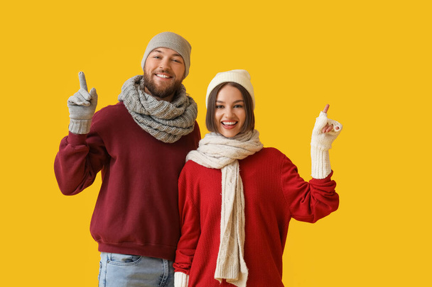 Glückliches junges Paar in stylischer Winterkleidung zeigt etwas auf farbigem Hintergrund - Foto, Bild