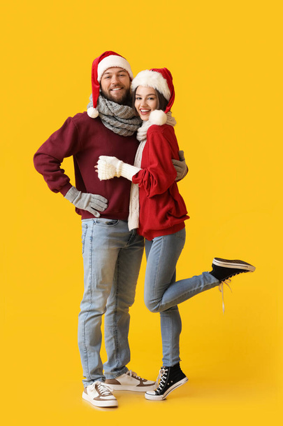 Ευτυχισμένο νεαρό ζευγάρι με κομψά χειμωνιάτικα ρούχα και καπέλα Αϊ-Βασίλη στο φόντο χρώμα - Φωτογραφία, εικόνα