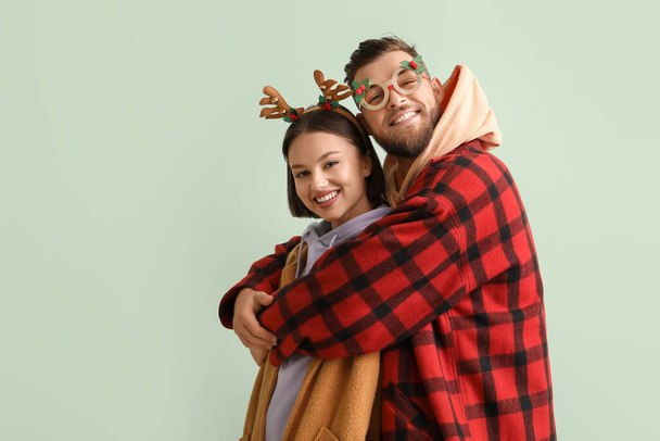 Szczęśliwa młoda para w stylowych zimowych ubraniach i z świątecznym wystrojem na jasnym tle - Zdjęcie, obraz