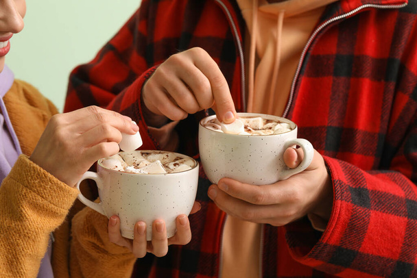 Молодая пара в зимней одежде и с чашками горячего шоколада на светлом фоне, крупным планом - Фото, изображение