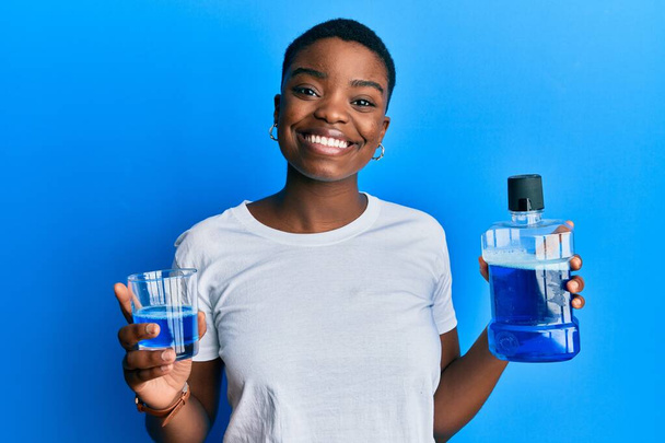 Young african american woman holding mouthwash for fresh breath smiling with a happy and cool smile on face. showing teeth.  - Fotoğraf, Görsel