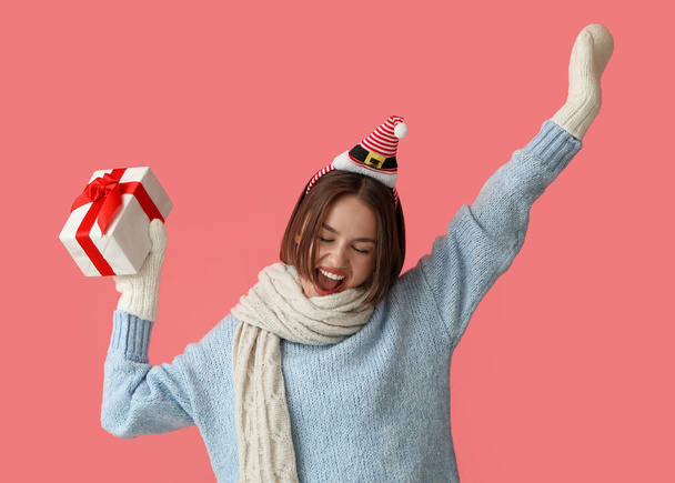 Happy young woman in stylish winter clothes and with Christmas gift on color background - Foto, Bild