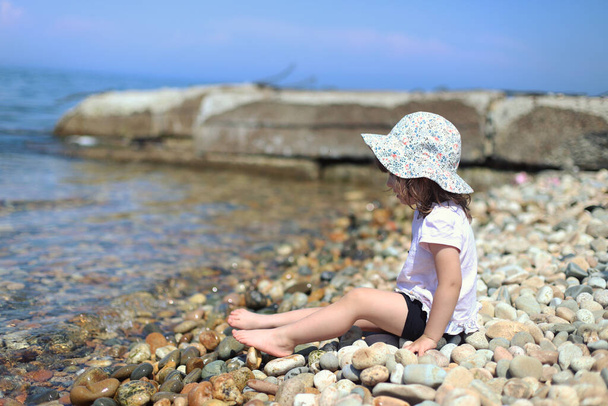 dark blonde girl in a white dress sits on a rocky beach by the sea - Foto, Bild