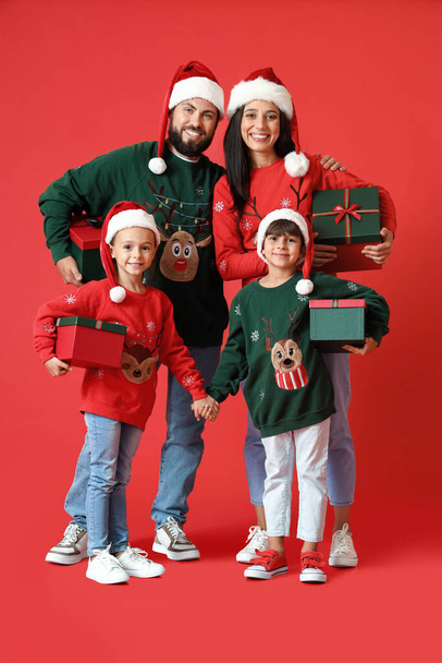 Happy family in Santa hats with Christmas gifts on red background - Zdjęcie, obraz