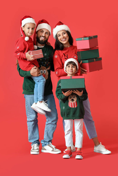Happy family in Santa hats with Christmas gifts on red background - Photo, Image