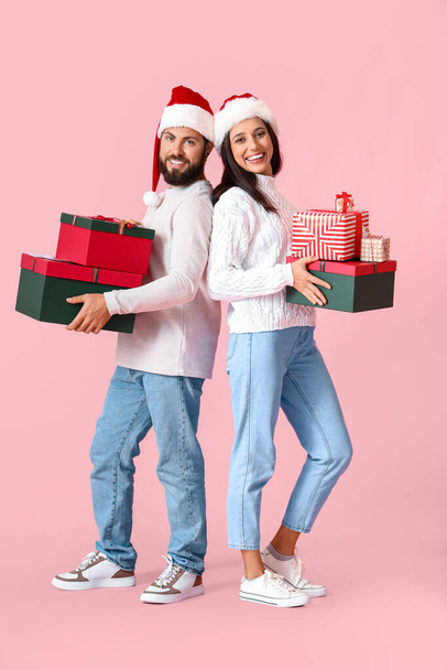 Happy young couple with Christmas gifts on pink background - Φωτογραφία, εικόνα
