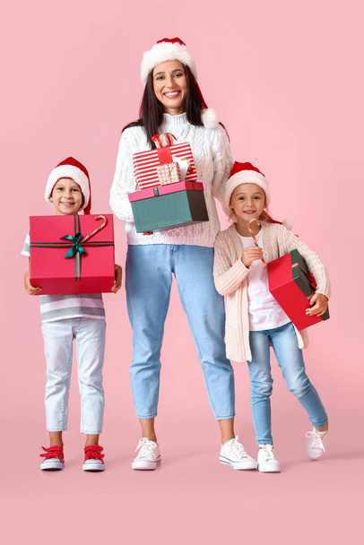 Młoda matka z małymi dziećmi i prezenty świąteczne na różowym tle - Zdjęcie, obraz