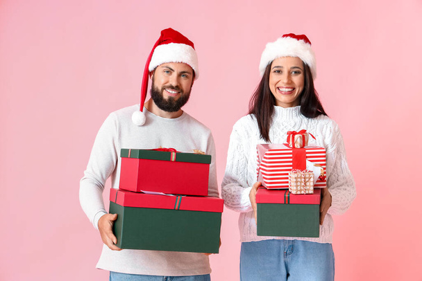 Happy young couple with Christmas gifts on pink background - Foto, Bild