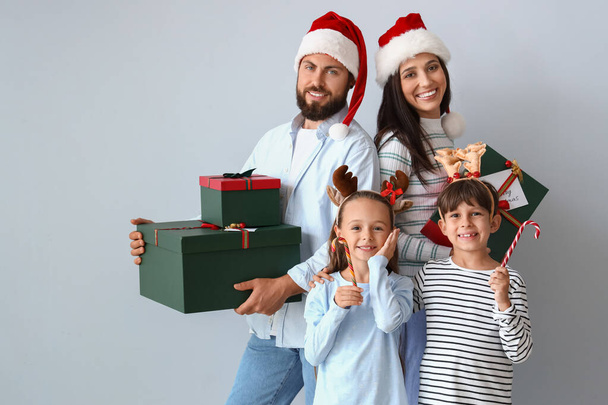 Happy family in Santa hats with Christmas gifts and candy canes on light background - Photo, Image