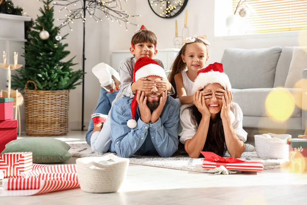 Niños pequeños cerrando los ojos a sus padres en casa en la víspera de Navidad - Foto, imagen