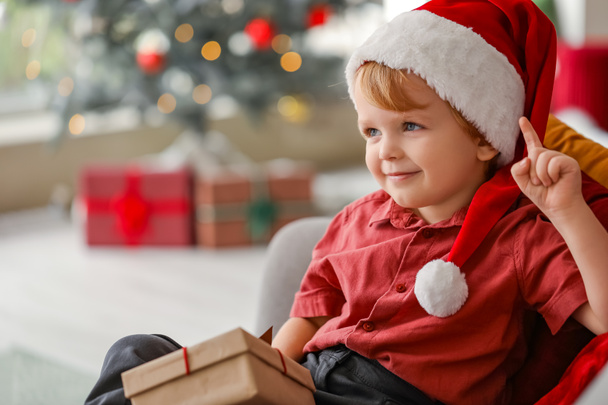 Little boy in Santa hat and with gift at home on Christmas eve - Photo, Image