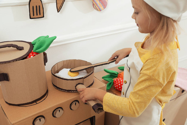 Little girl playing with toy cardboard kitchen indoors, closeup - Zdjęcie, obraz