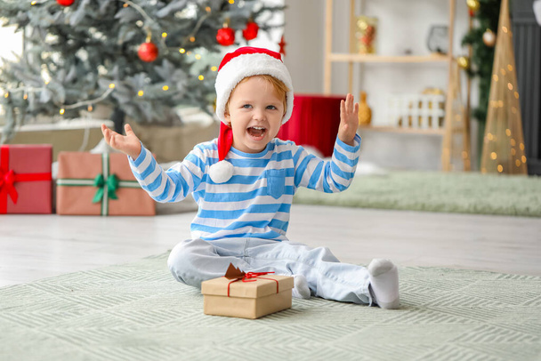 Little boy in Santa hat and with gift at home on Christmas eve - Photo, image