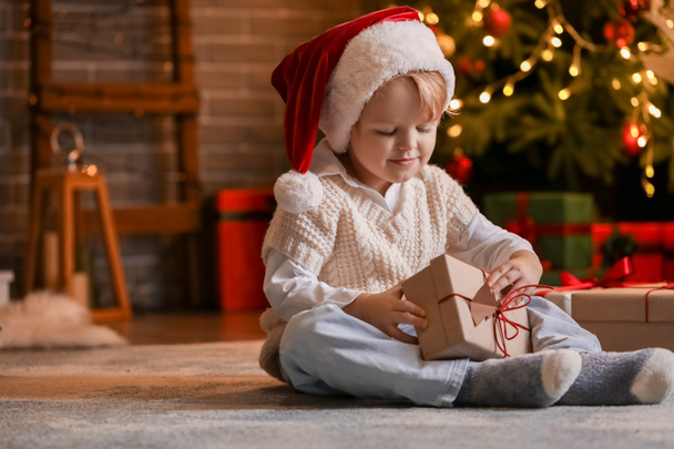 Kleine jongen in Santa hoed en met kerstcadeau thuis - Foto, afbeelding