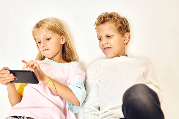 κορίτσι με ένα τηλέφωνο στα χέρια της δίπλα σε ένα αγόρι που παίζει παιχνίδια - Φωτογραφία, εικόνα