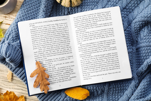 Beautiful autumn composition with book, sweater and leaves on white wooden background - Foto, imagen