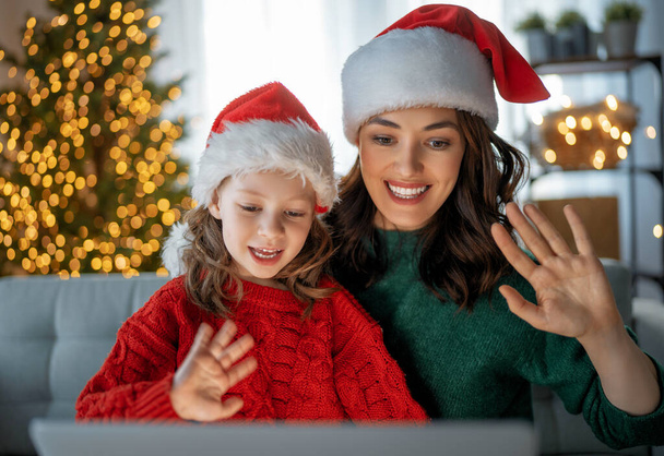 Mother and daughter are chatting with somebody using laptop in the living room decorated for Christmas. - Foto, afbeelding