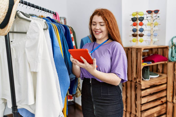 Giovane donna rossa utilizzando touchpad di lavoro presso il negozio di abbigliamento - Foto, immagini