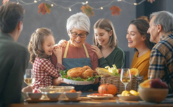 Thanksgiving Day, Autumn feast. Happy family sitting at the table and celebrating holiday. Grandparents, mother, father and children. Traditional dinner. - 写真・画像