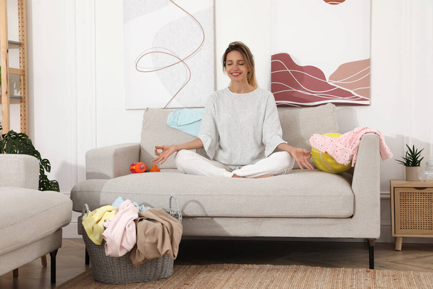 Young mother meditating on sofa in messy living room - Foto, Bild