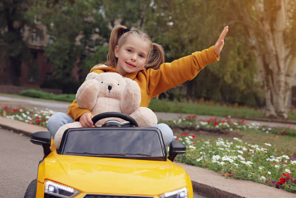 Cute little girl with toy bear driving children's car in park - Fotó, kép