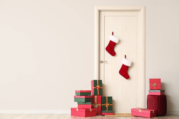 Φωτεινή ξύλινη πόρτα με χριστουγεννιάτικες κάλτσες και κουτιά δώρων στο δωμάτιο - Φωτογραφία, εικόνα