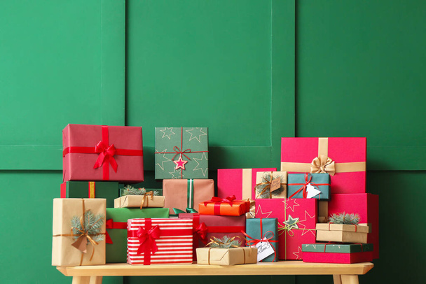 Ξύλινο τραπέζι με χριστουγεννιάτικα δώρα κοντά σε πράσινο τοίχο - Φωτογραφία, εικόνα