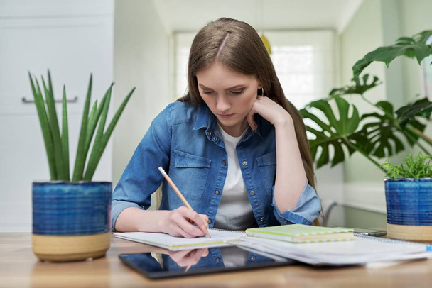 Female university student studies at home, writes in a notebook - Foto, afbeelding