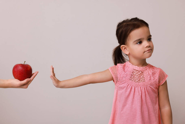 Cute little girl refusing to eat apple on grey background - Valokuva, kuva
