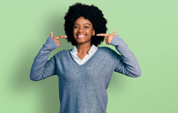 Jeune femme afro-américaine portant des vêtements de travail souriant et joyeux montrant et pointant du doigt les dents et la bouche. concept de santé dentaire.  - Photo, image