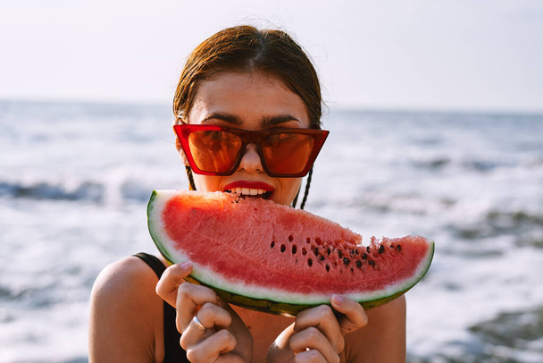 cheerful woman in sunglasses eating watermelon by the ocean - Foto, afbeelding