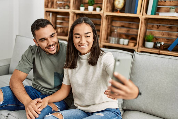 Giovane coppia latina sorridente felice fare selfie dallo smartphone a casa. - Foto, immagini