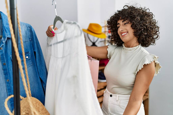 若い中東の顧客女性は、衣料品店でシャツとハンガーを保持. - 写真・画像