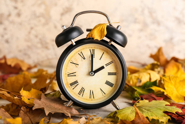 Alarm clock and autumn leaves on grunge background. Daylight saving time end - Photo, Image