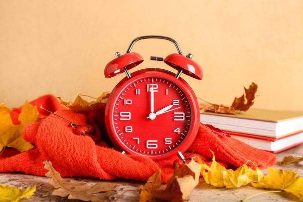 Alarm clock and autumn leaves with clothes on color background. Daylight saving time end - Photo, Image