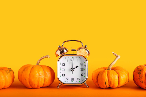 Alarm clock and pumpkins on color background. Daylight saving time end - Photo, Image