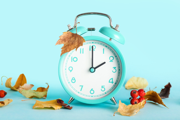 Reloj despertador y hojas de otoño sobre fondo azul. Fin del horario de verano - Foto, imagen