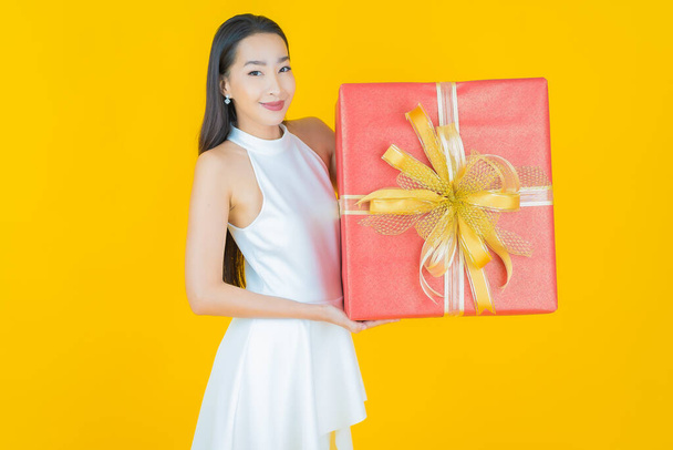 Portrait beautiful young asian woman smile with red gift box on color background - 写真・画像