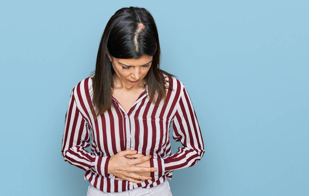 Beautiful brunette woman wearing striped shirt with hand on stomach because indigestion, painful illness feeling unwell. ache concept.  - Foto, immagini