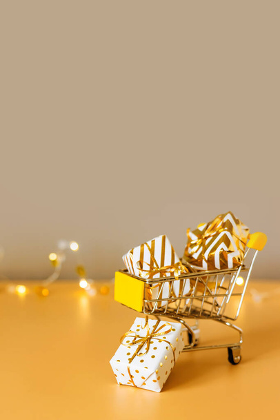 Shopping e vendita di Natale online. Carrello con scatole regalo su sfondo dorato con luci. Carrello supermercato pieno di regali. Banner con spazio di copia - Foto, immagini