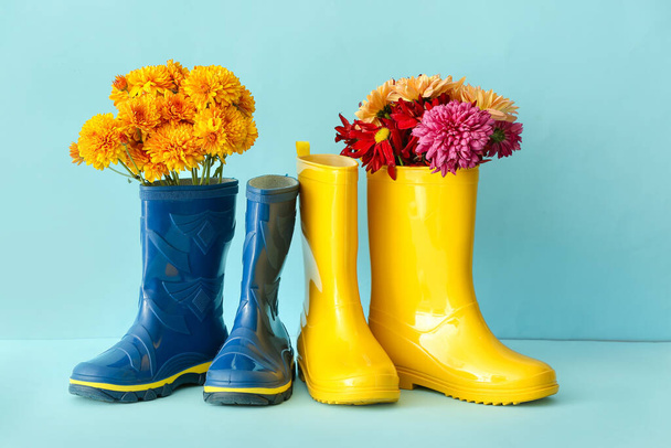 Rubber boots and beautiful autumn flowers on color background - Fotografie, Obrázek
